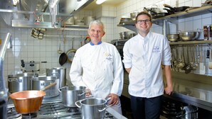Two chefs in a kitchen with stainless steel appliances, pots, and pans on the counter. - Hôtel Gruber (Rosport-Mompach)