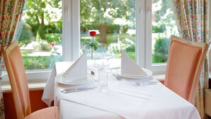 A dining table set for two with a white tablecloth, two chairs, and a vase with a single red rose. - Hôtel Gruber (Rosport-Mompach)