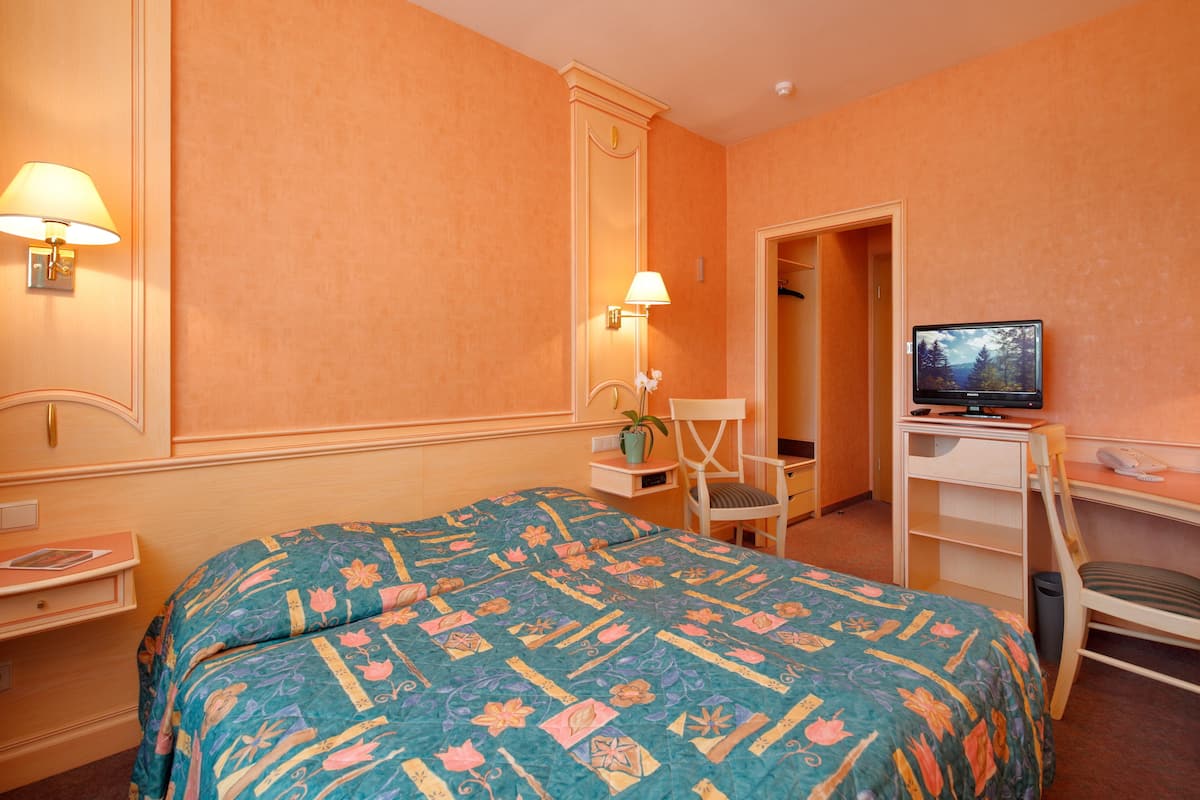 Una habitación de hotel con cama, escritorio, silla, televisor y espejo.