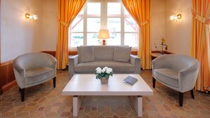 A room with a sofa, two armchairs, a coffee table, and a window with curtains. - Hôtel Gruber (Rosport-Mompach)