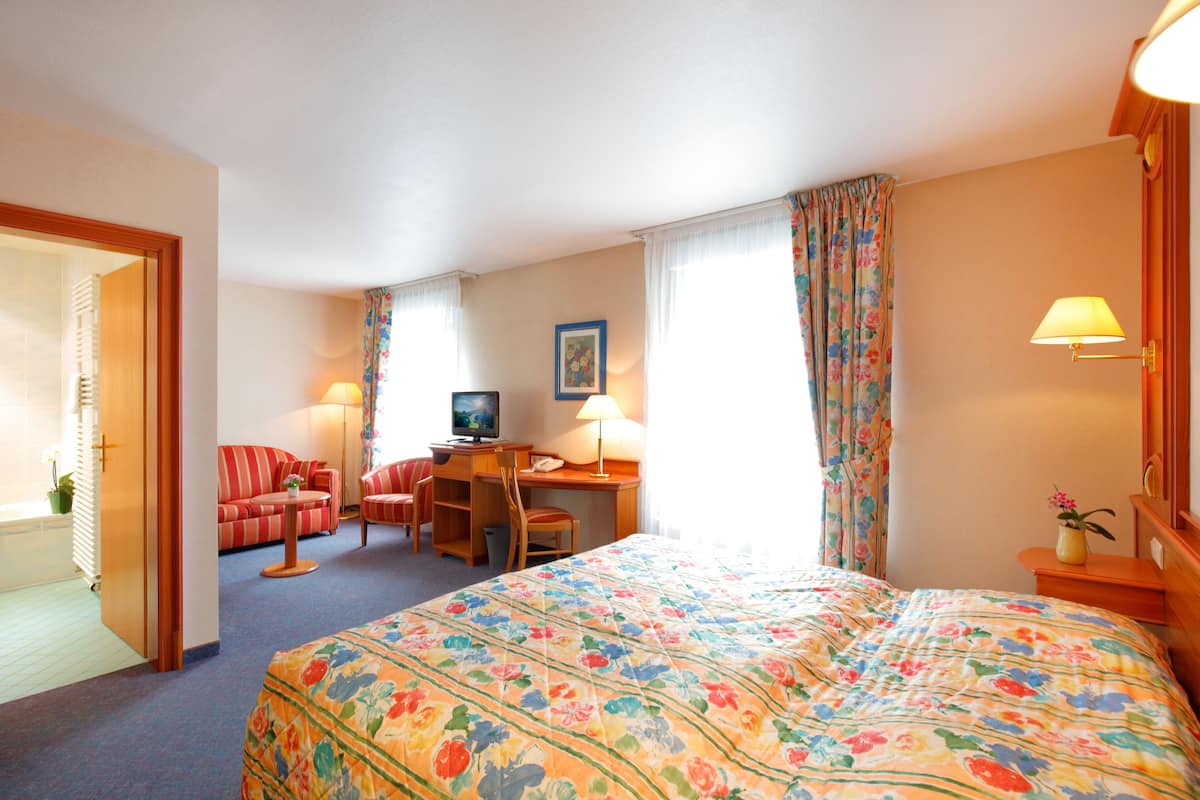 Una habitaci ón de hotel con cama, escritorio, silla, televisor y lámpara.