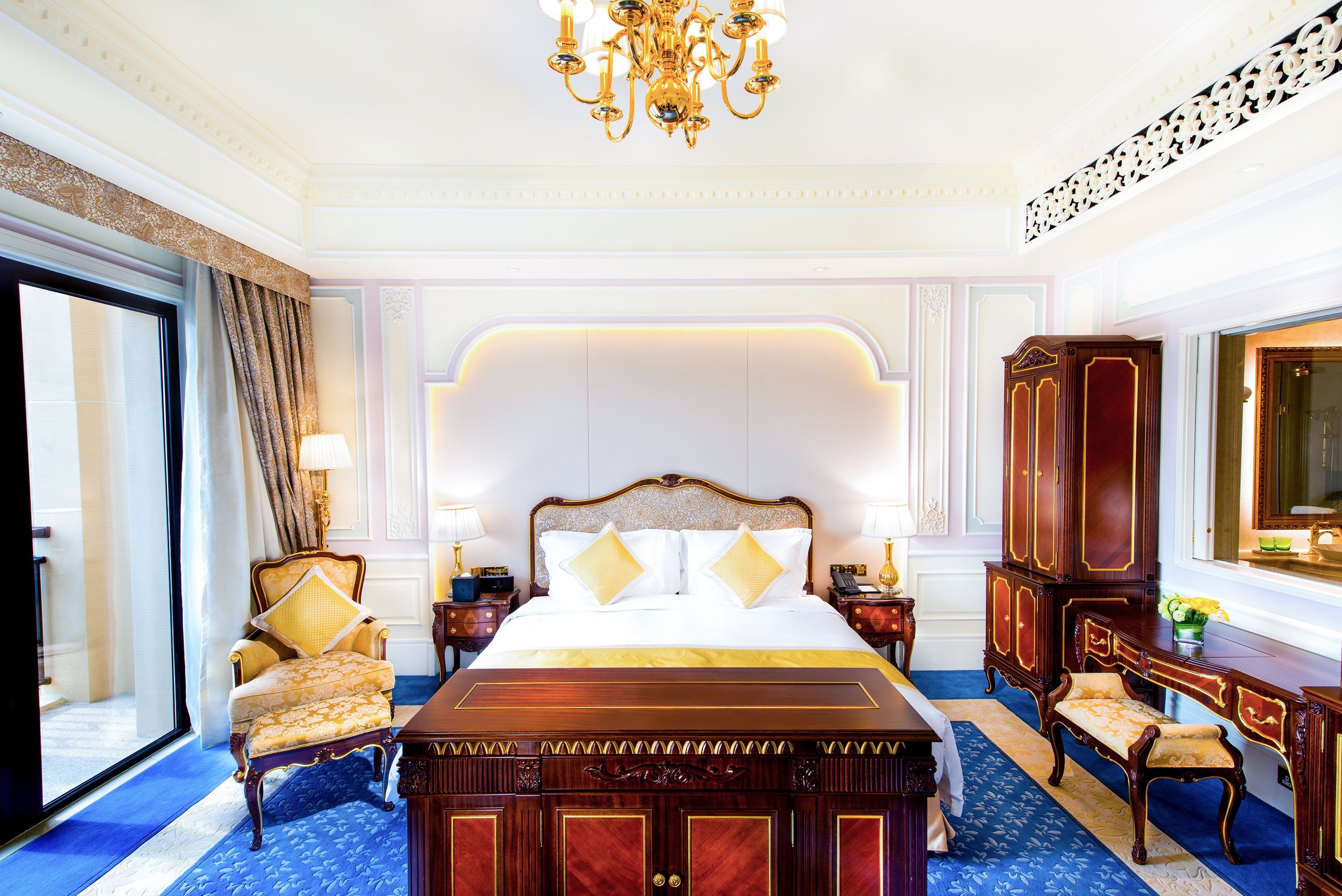 A luxurious bedroom with a large bed, ornate wooden furniture, and a chandelier.