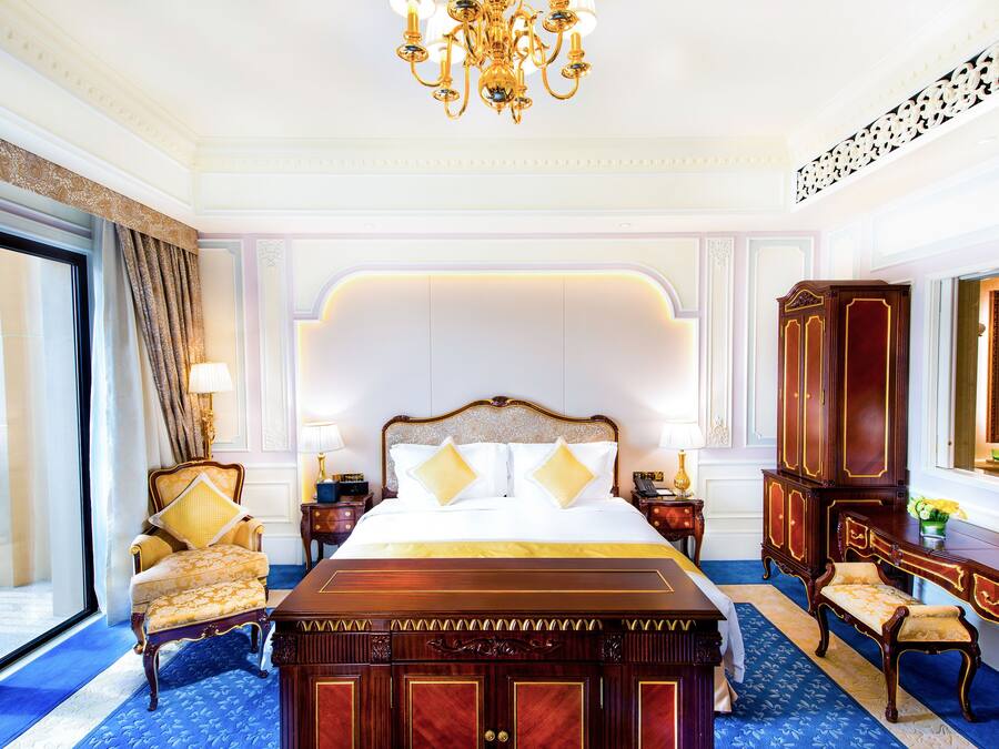 A luxurious bedroom with a large bed, ornate wooden furniture, and a chandelier.