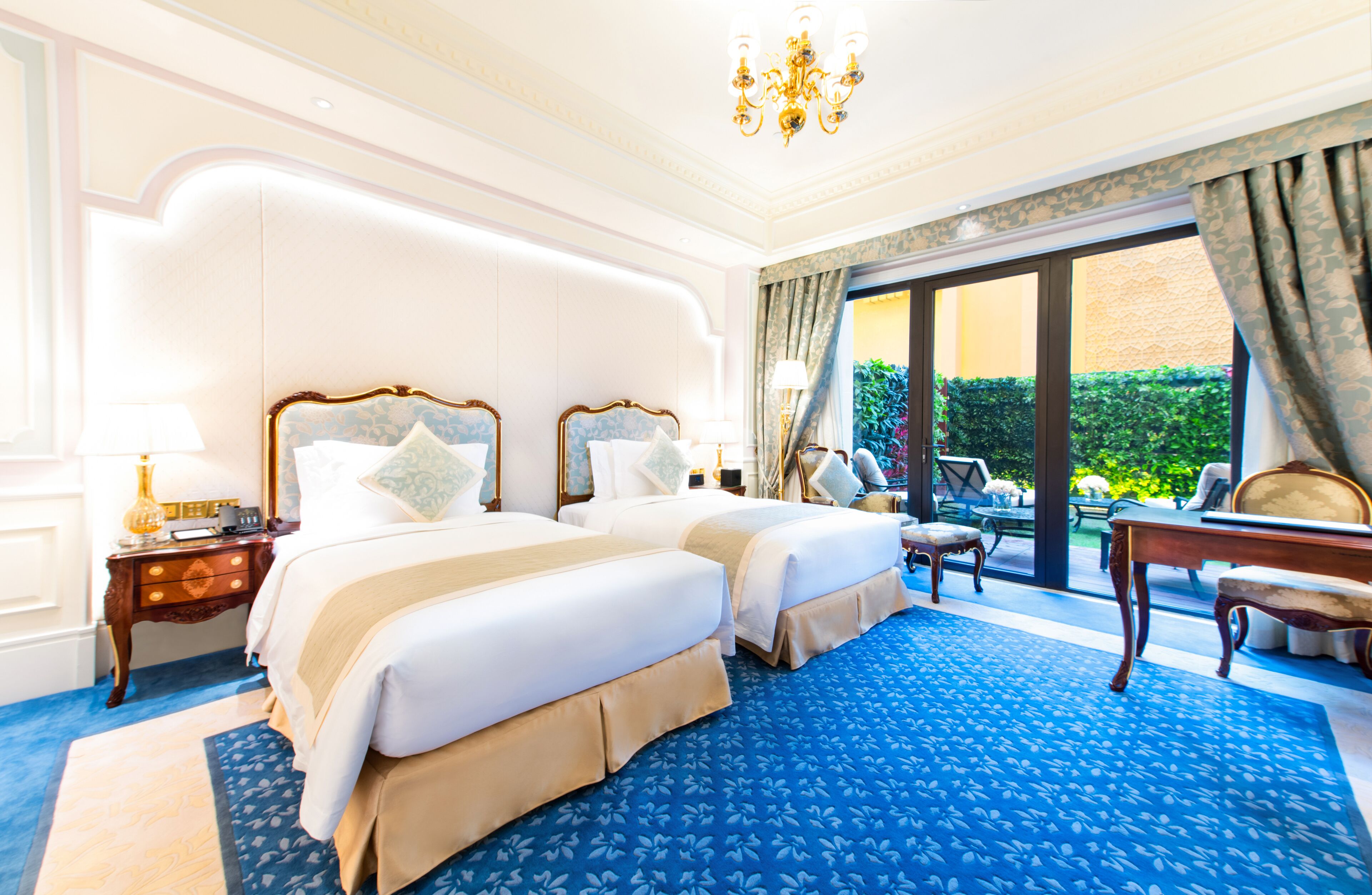 Une chambre d’hôtel avec deux lits, une grande fenêtre donnant sur un beau paysage, un lustre et une moquette bleue.