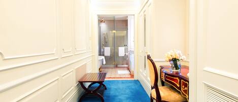 Un couloir étroit avec une moquette bleue, un banc en bois, une chaise et une petite table.