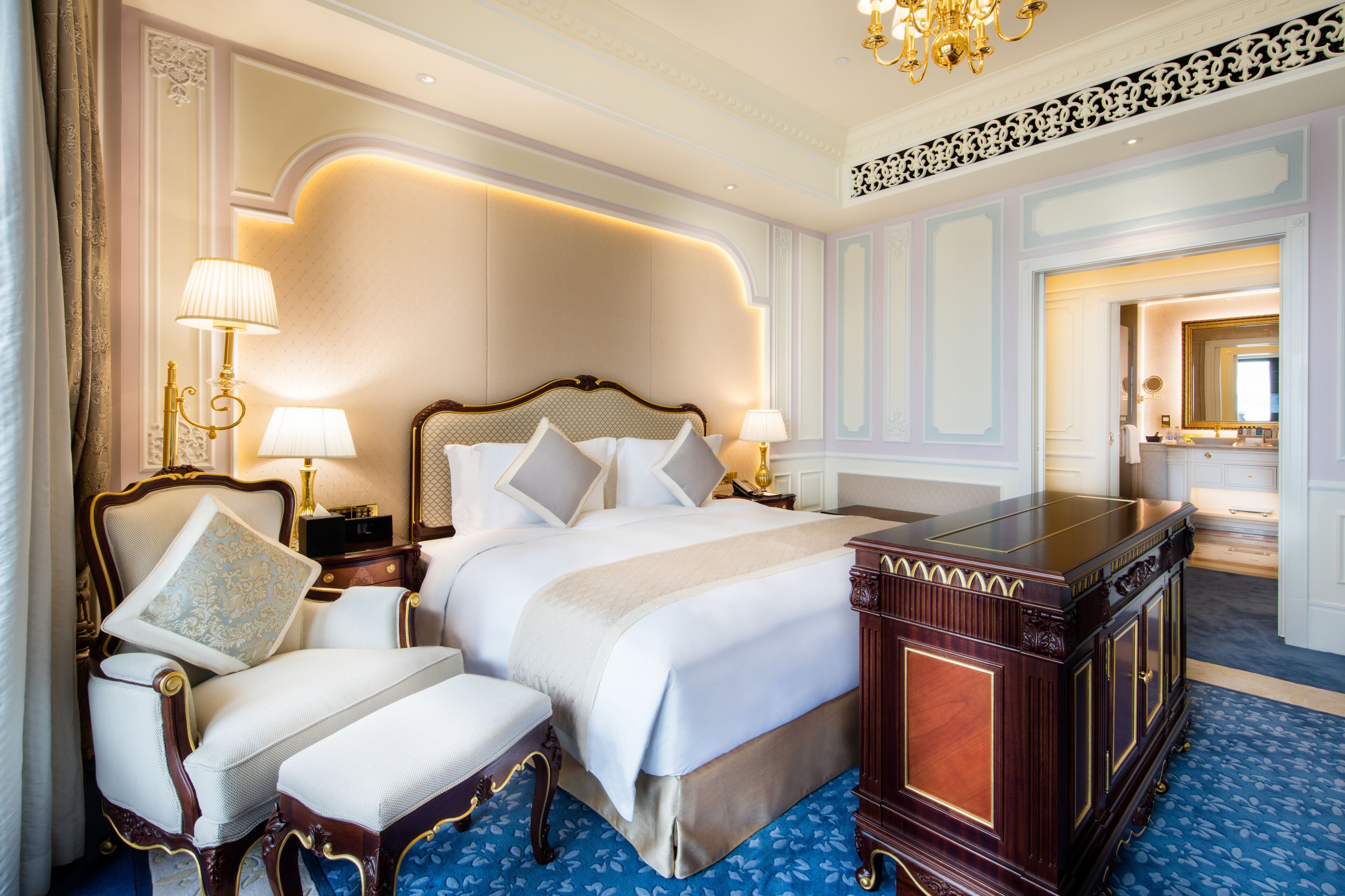 A luxurious bedroom with a large bed, two bedside tables with lamps, a wooden dresser, and a chair.