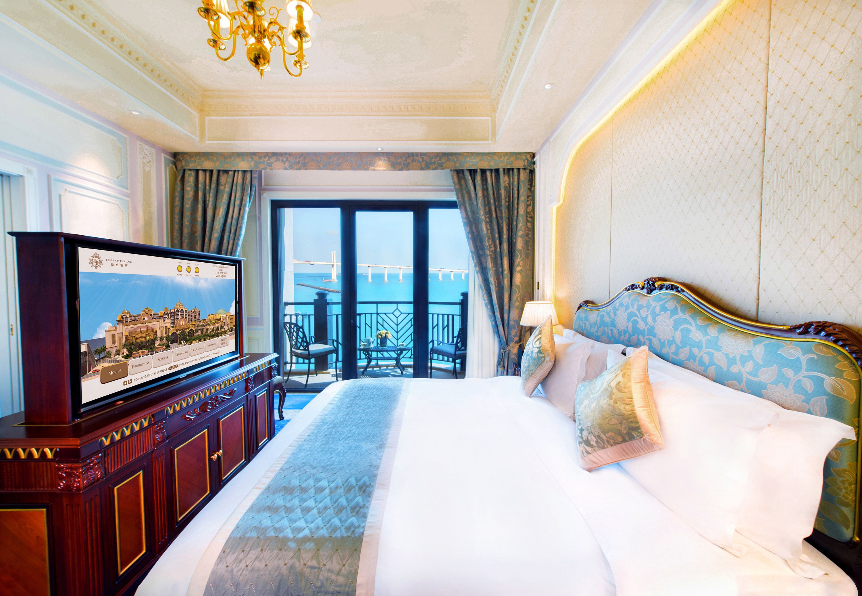 A hotel room with a large bed, a television on a wooden cabinet, and a balcony with a view of a bridge.