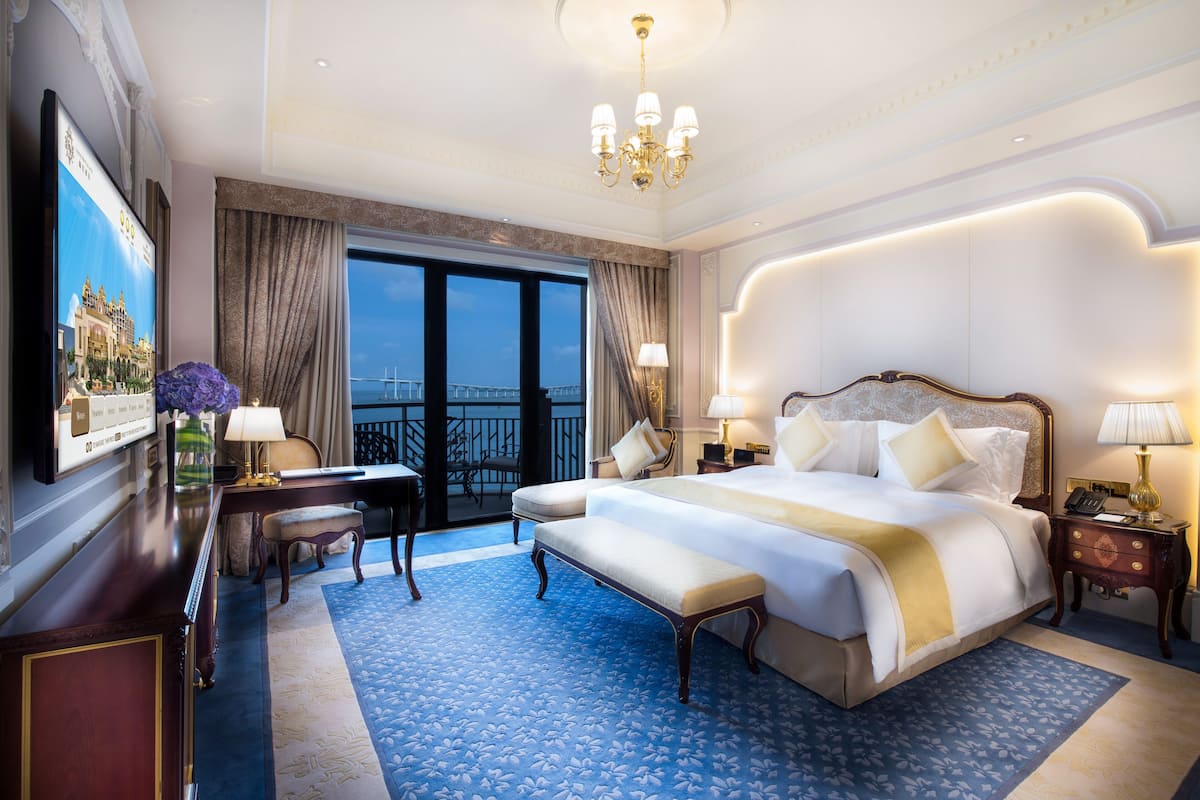 A spacious hotel room with a large bed, a desk, and a view of the cityscape through the window.