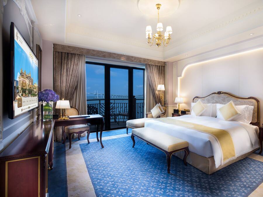 A spacious hotel room with a large bed, a desk, and a view of the cityscape through the window.