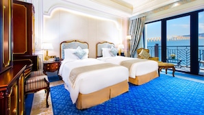 A luxurious hotel room with two large beds, a sitting area with a chair, a desk, and a view of a bridge. - Legend Palace Hotel (Macau)