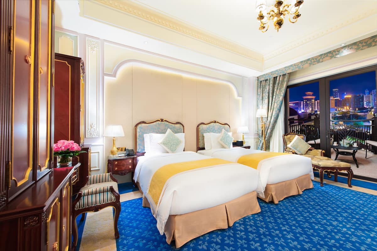 A hotel room with two beds, a nightstand, a chair, and a view of the cityscape at night.