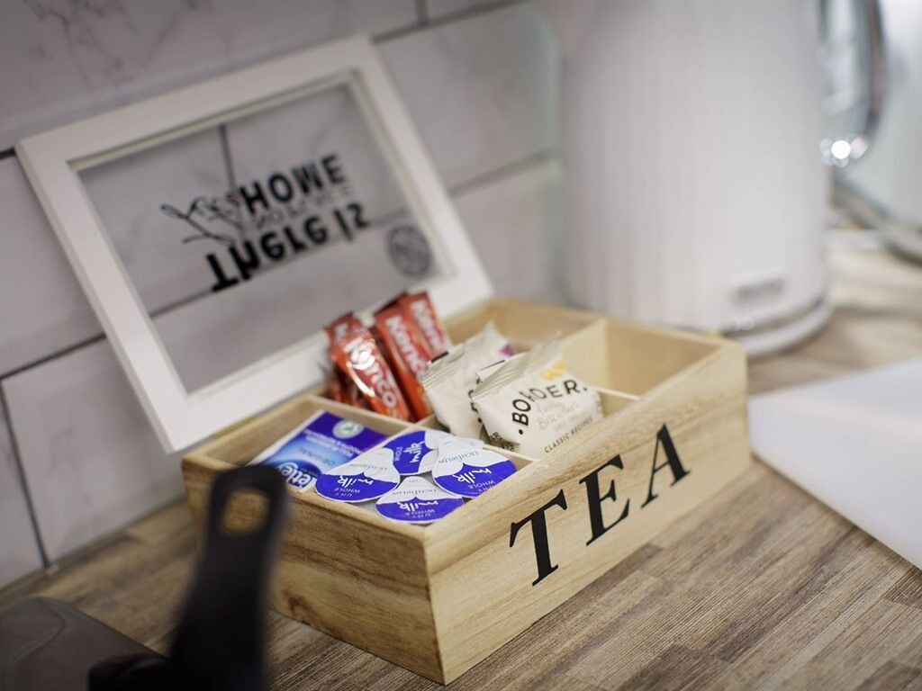 Une boîte en bois étiquetée « THÉ », contenant divers sachets de thé, et un panneau encadré en arrière-plan.