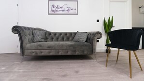 A grey tufted sofa with patterned cushions, a black chair with gold legs, and a framed artwork on the wall. - Fewston House Apartments (Leeds)