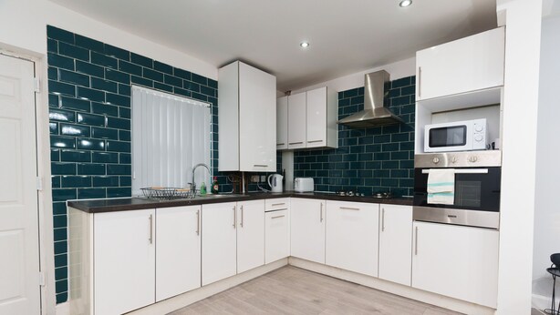 A modern kitchen with white cabinets, a stainless steel range hood, a microwave, and a built-in oven. - Fewston House Apartments (Leeds)