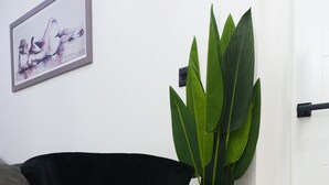 A black chair with wooden legs, a potted plant, and a framed artwork on a white wall. - Fewston House Apartments (Leeds)