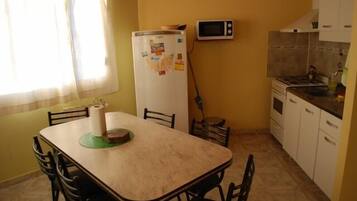 A compact kitchen with a refrigerator, microwave, and stove. There is a dining table with chairs.