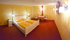 A hotel room with a bed, bedside table, lamp, chair, and a small round table with a tablecloth. - Gotikhotel Frenzelhof (Görlitz)