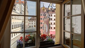 A room with a large bay window overlooking a street with buildings and a sign for a restaurant. - Gotikhotel Frenzelhof (Görlitz)