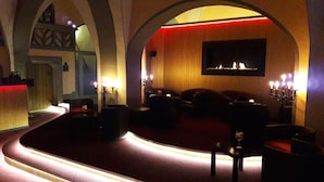 A dimly lit lounge area with a curved seating arrangement, a chandelier, and a wall-mounted TV. - Gotikhotel Frenzelhof (Görlitz)