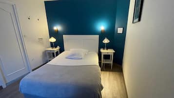 A bedroom with a large bed, two bedside tables with lamps, a white headboard, and a blue accent wall.