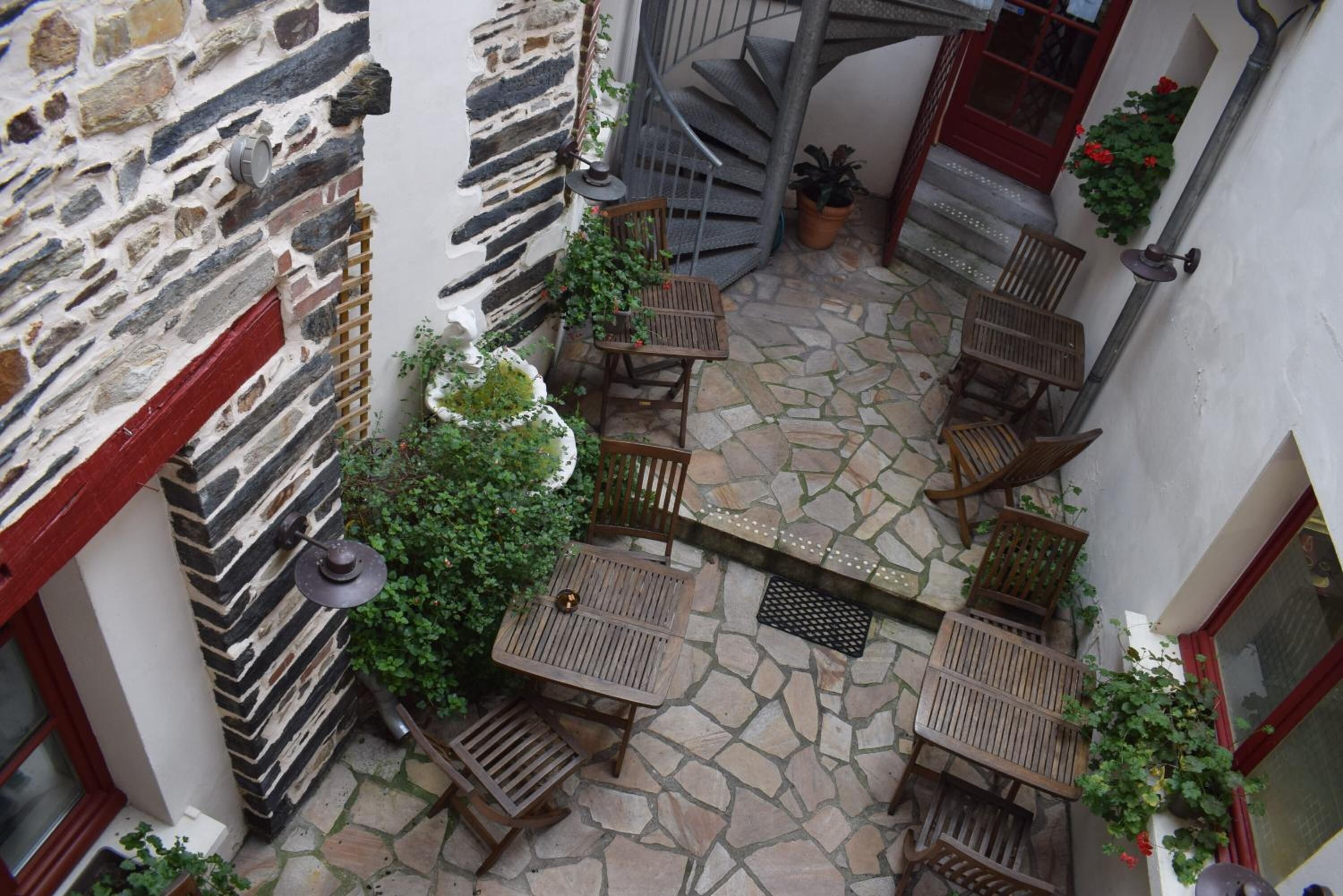 A courtyard with stone flooring, wooden furniture, and a spiral staircase.