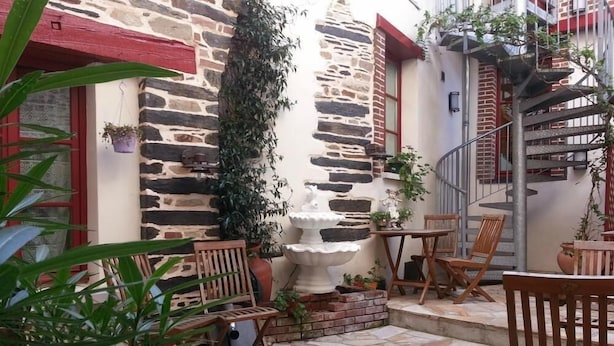 A stone-floored patio with wooden chairs and tables, surrounded by potted plants and a decorative fountain. - Hotel du Chateau (Vitre)
