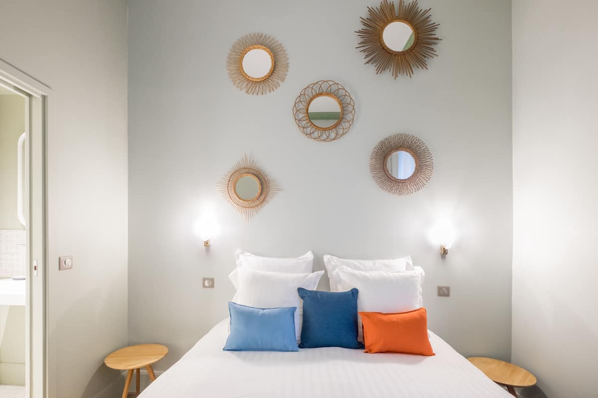 A hotel room with a bed, pillows, and wall-mounted mirrors.