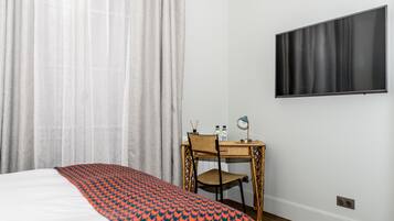 A hotel room with a bed, a desk with a chair, a flat-screen TV, and a window with curtains.