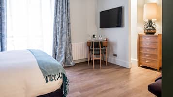 A hotel room with a bed, a desk, a chair, a TV, a lamp, and a dresser.
