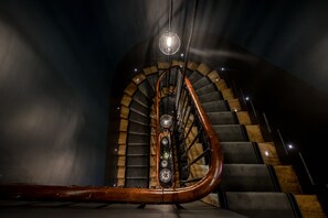 Una scala a chiocciola con gradini in legno e una ringhiera centrale, che sale in una stanza scarsamente illuminata.