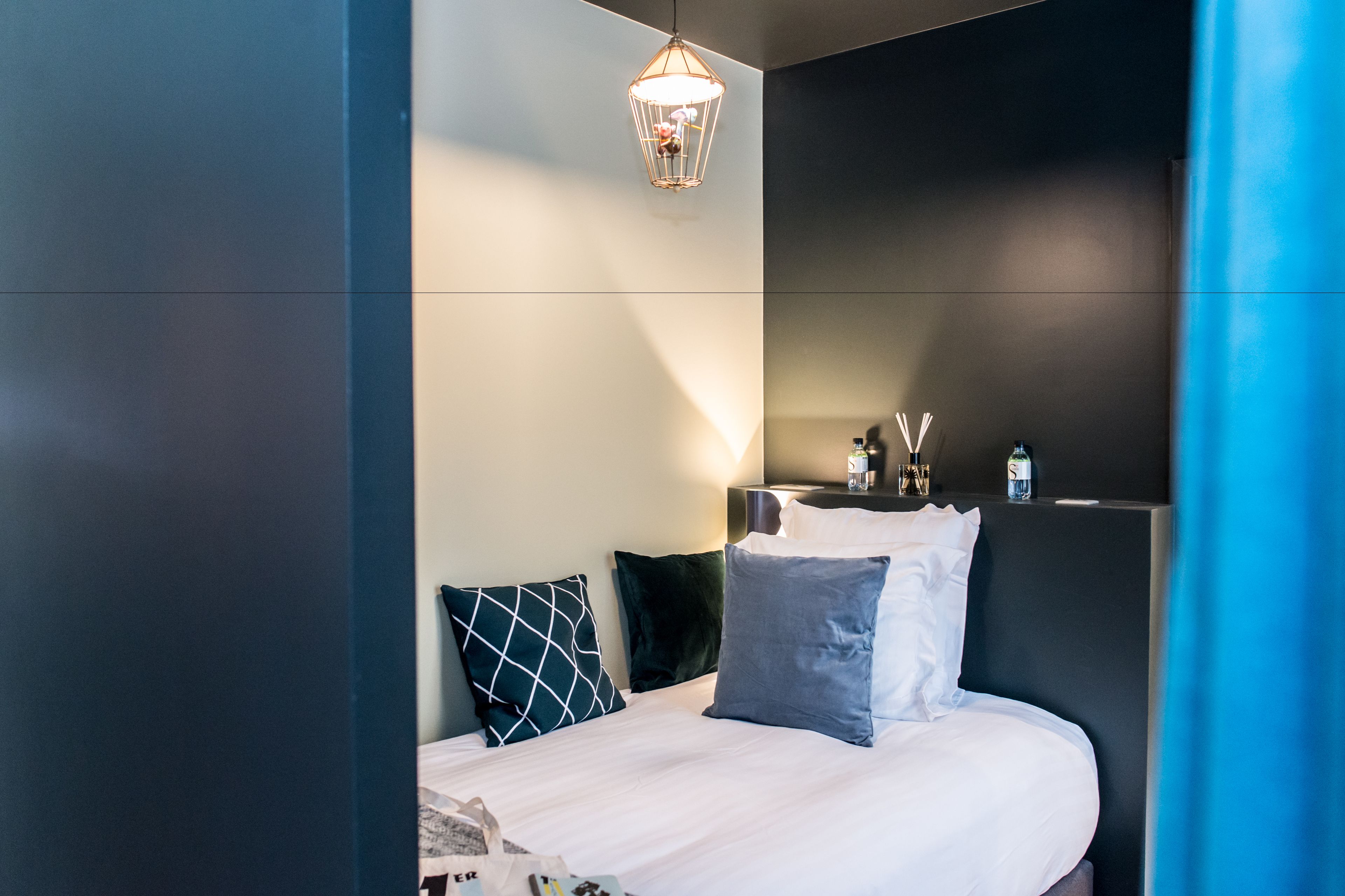 A modern hotel room with a neatly made bed, a bedside table with a lamp, and a wall-mounted TV.