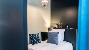 A modern hotel room with a neatly made bed, a bedside table with a lamp, and a wall-mounted TV.