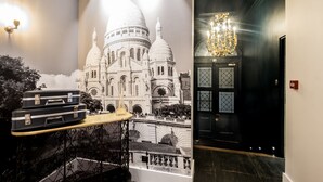 A room with a large mural of a cathedral, a chandelier, and two suitcases on a table.