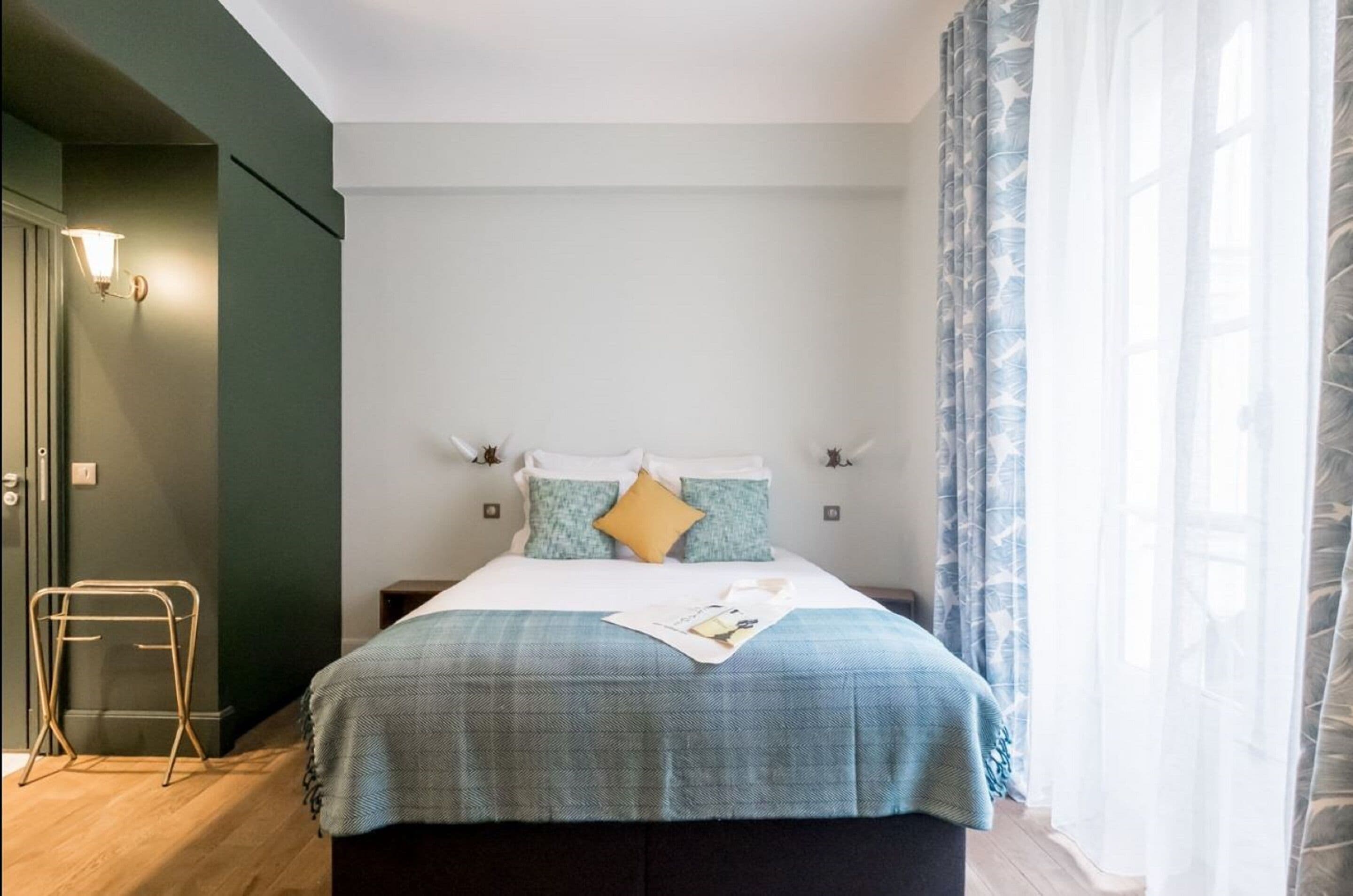 Un lit bien fait, recouvert d’une couverture à carreaux bleus et blancs, avec deux oreillers et un magazine posé sur le lit.