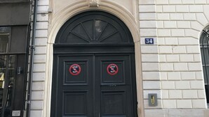 A building with a black double door, a balcony with white shutters, and a sign indicating the number 34.