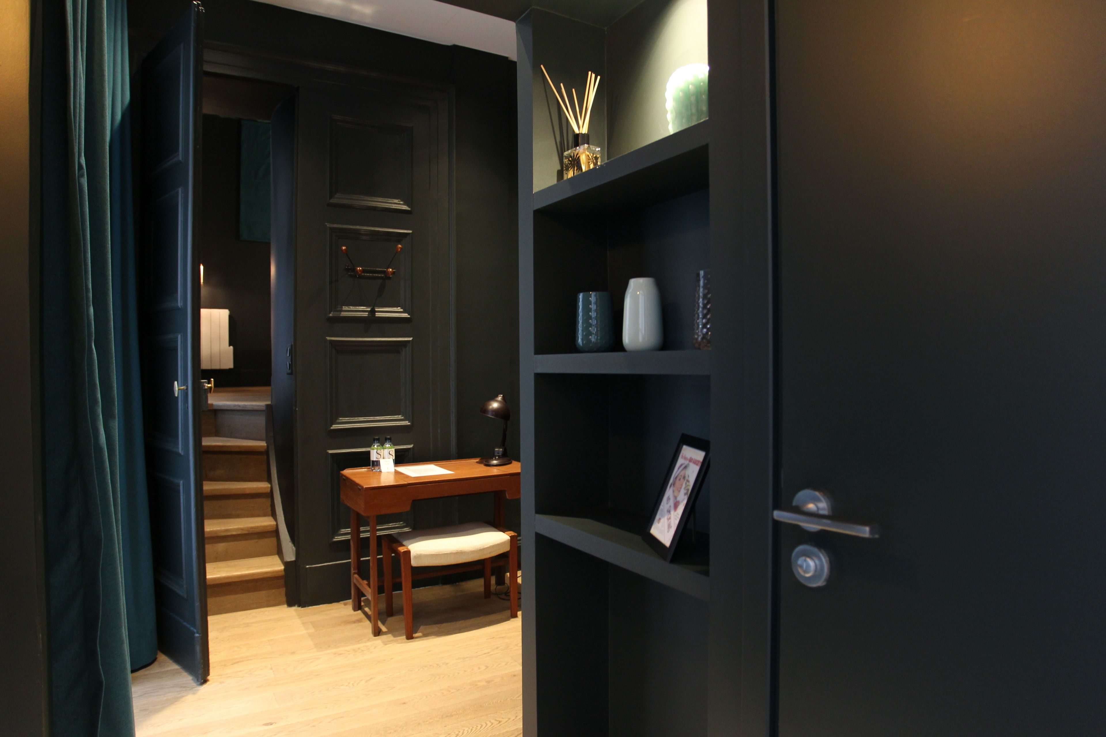 Een donkere kamer met een bureau, stoel en planken met decoratieve objecten.