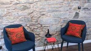 Two dark blue chairs with red patterned cushions, a small round mirror, and a decorative metal stand with a red book on a stone wall.