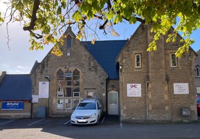 A stone building with a car parked in front, signs for 'Busy Bodies Childcare Centre' and 'Athena Greek Tavern and Cafe'.