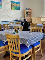 A restaurant with wooden chairs and tables covered with checkered tablecloths. There are wine glasses and bottles on the tables.