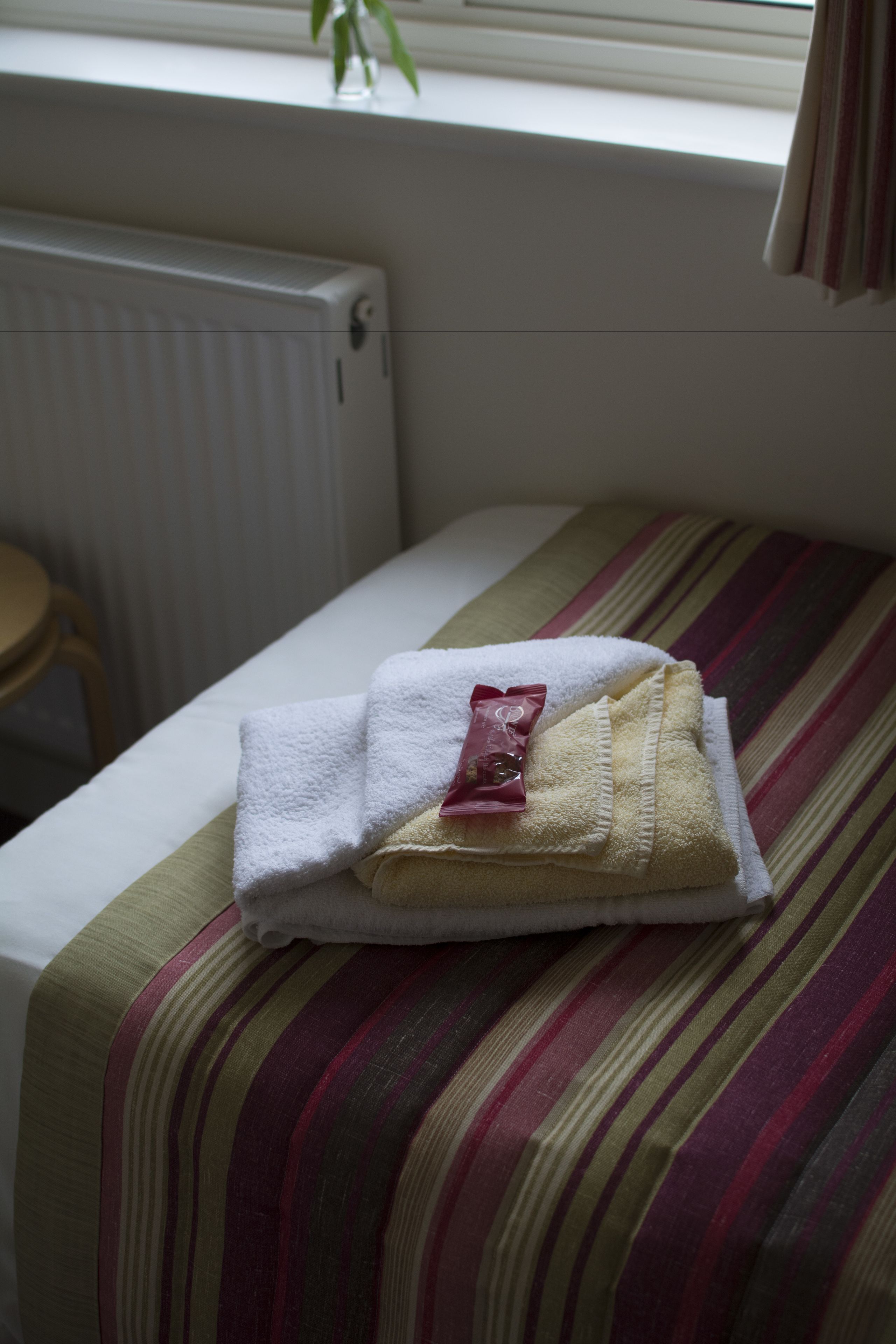 Una cama bien hecha con una colcha a rayas, una toalla blanca doblada y un paquete rojo sobre la cama.
