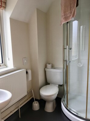 Un baño con inodoro, bidé, lavamanos y ducha con mampara de vidrio.