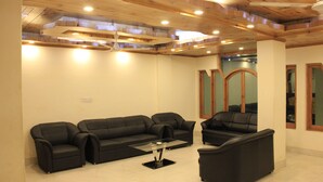 Una sala de estar moderna con techo de madera, dos sofás negros, una mesa de centro de vidrio y una mesita auxiliar.