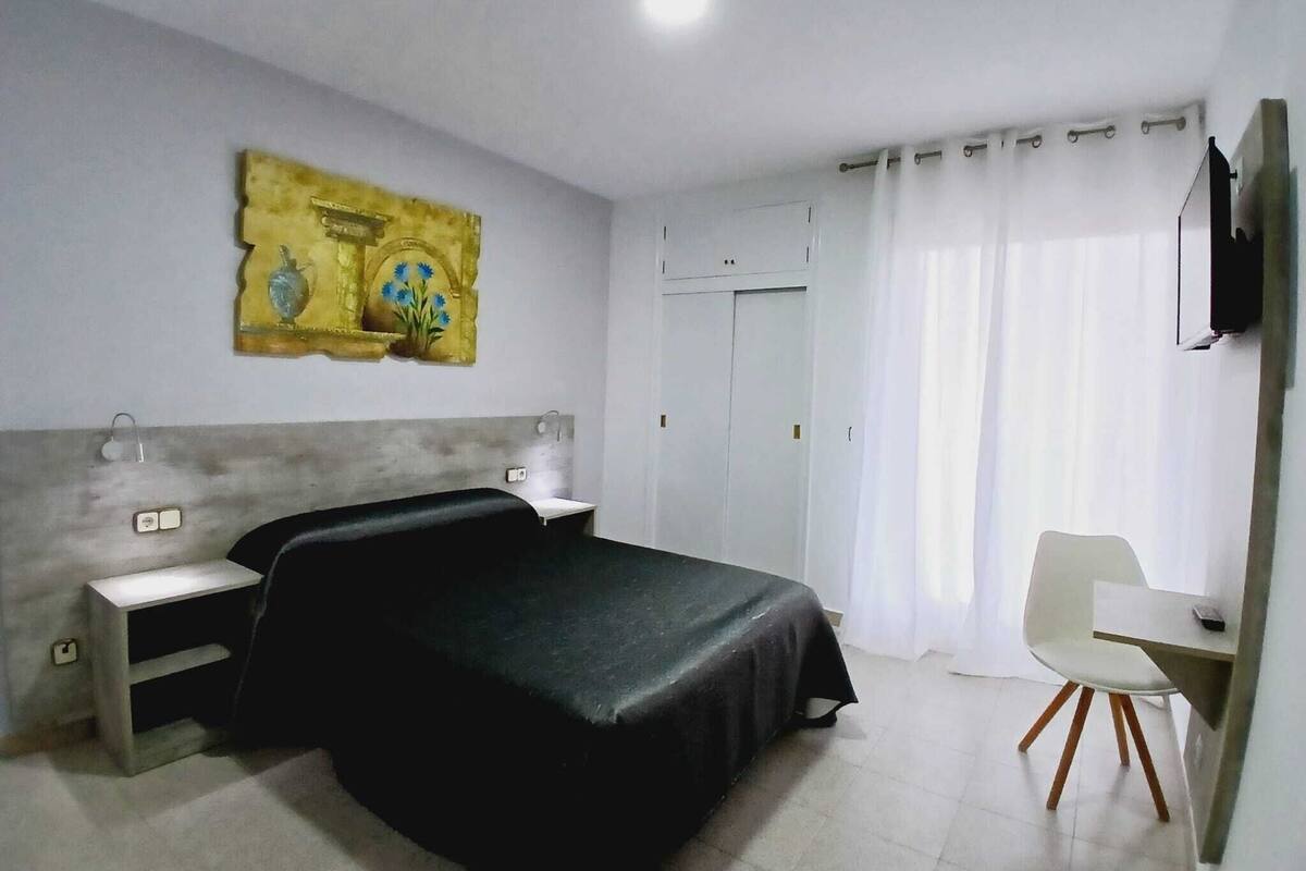 Une chambre d’hôtel avec un lit, un bureau, une chaise, une télévision et un tableau au mur.