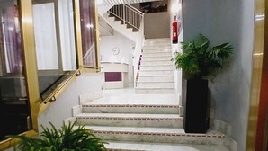 Una escalera de mármol con barandilla que lleva a un rellano con un reloj y un extintor.