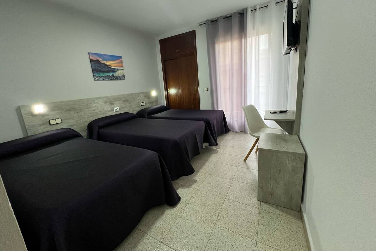 Une chambre d’hôtel avec deux lits, un bureau, une chaise, une télévision et un tableau au mur.