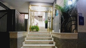 Una escalera conduce a la entrada de un edificio, con una reja metálica a la izquierda y una planta en maceta al final.