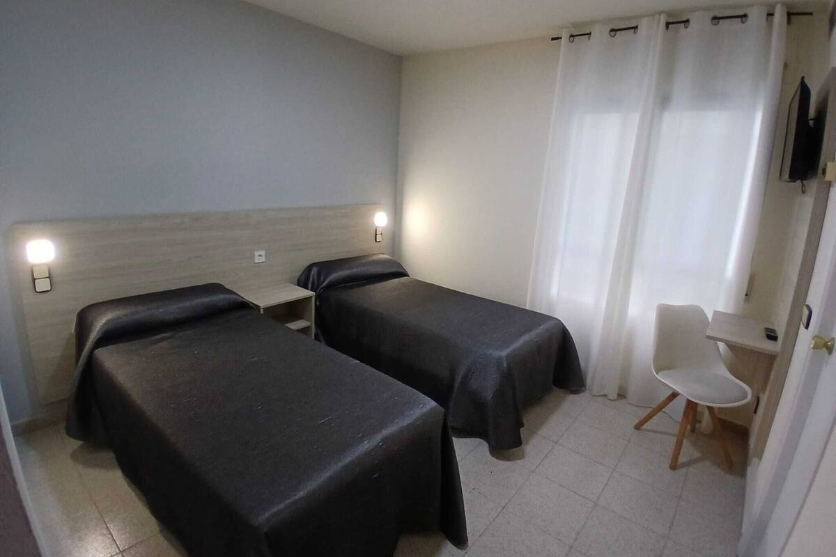 Une petite chambre d’hôtel avec deux lits simples, un bureau avec une chaise et un téléviseur fixé au mur.