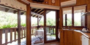 Una cabaña de madera con área de cocina, una mesa de comedor y una terraza con vistas a la vegetación.