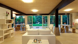 A modern living room with a white sofa, wooden tables, and a glass door leading to a garden. - Las casas de Ea Astei (Ea)