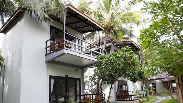 A modern two-story building with a balcony, surrounded by lush greenery and a paved pathway. - Salty River Resort (Kampot)